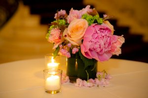 A picture of a floral arrangement with rose, yellow, and pastel colors on a table next to candles