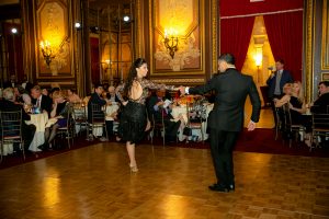 A man and a woman are dancing alone on the ballroom while seated guests watch